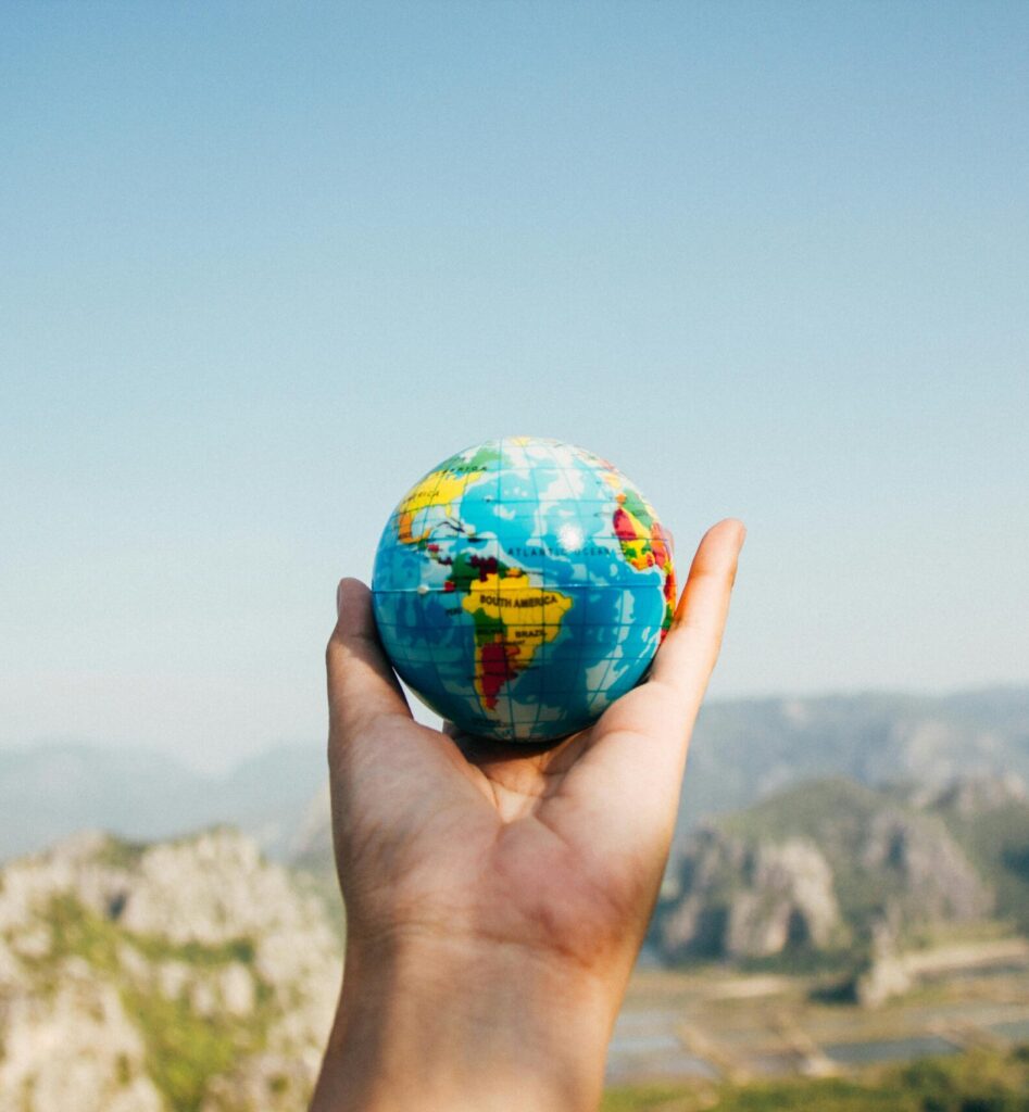 Person Holding World Globe Facing Mountain